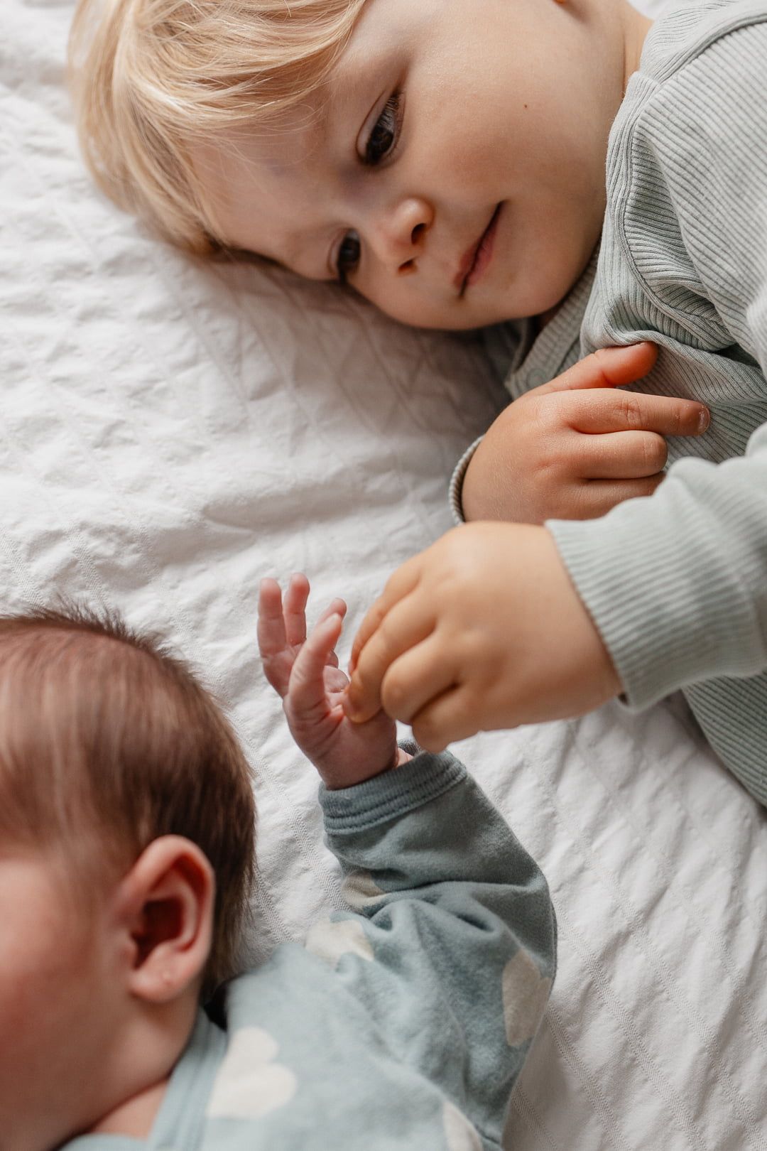 adorable photo capturee en shooting naissance a domicile a Lille : un grand frere compte les doigts minuscules de sa petite soeur