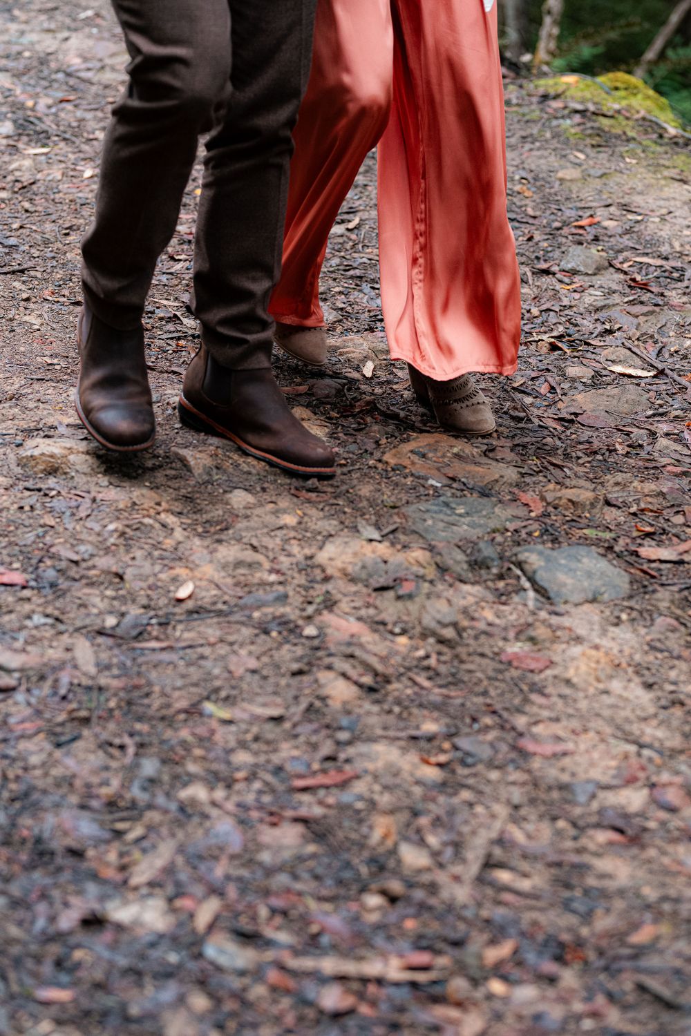Close-up of feet wearing brown boots and coral-colored pants standing on a rocky forest path.