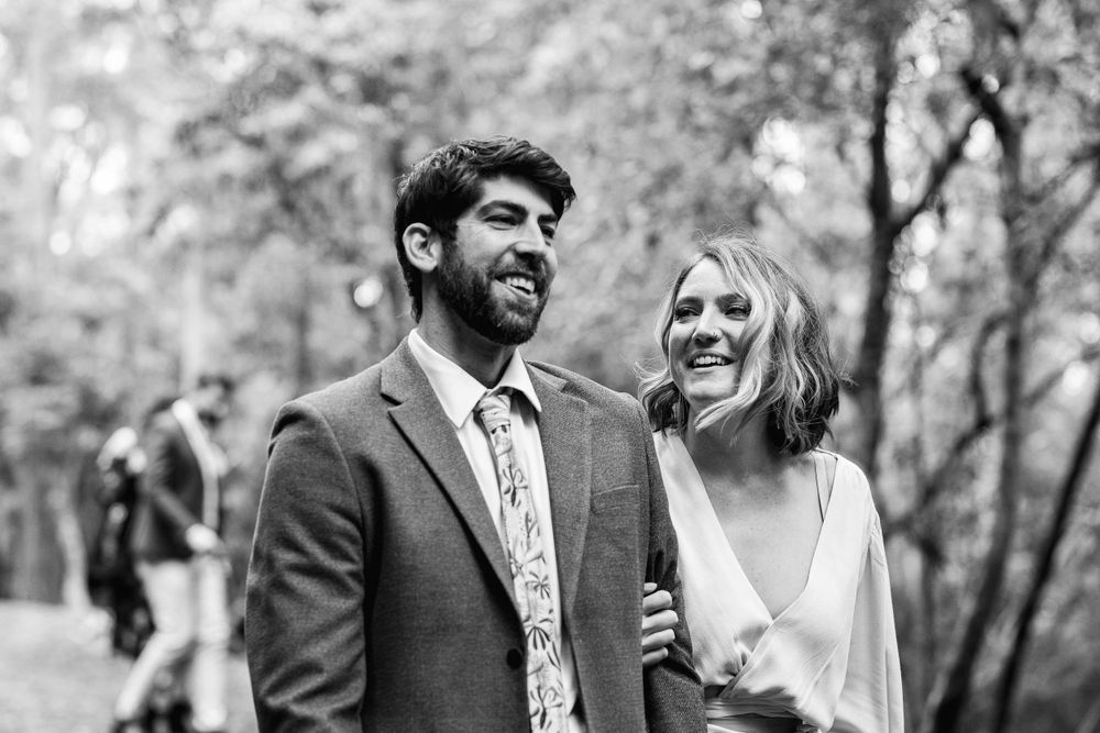 A joyful black and white portrait of a couple sharing a candid moment in a wooded setting.