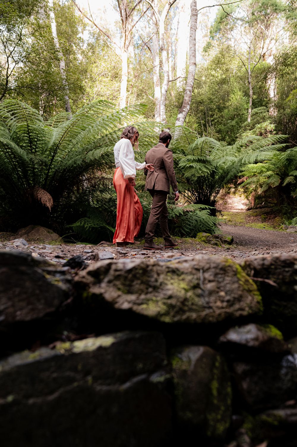 A couple sharing an intimate moment among giant ferns in a lush forest setting.