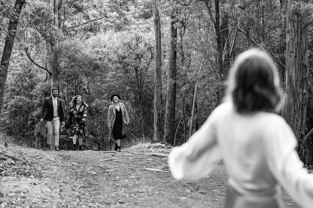 A black and white photograph of people meeting on a forest path during a casual gathering.