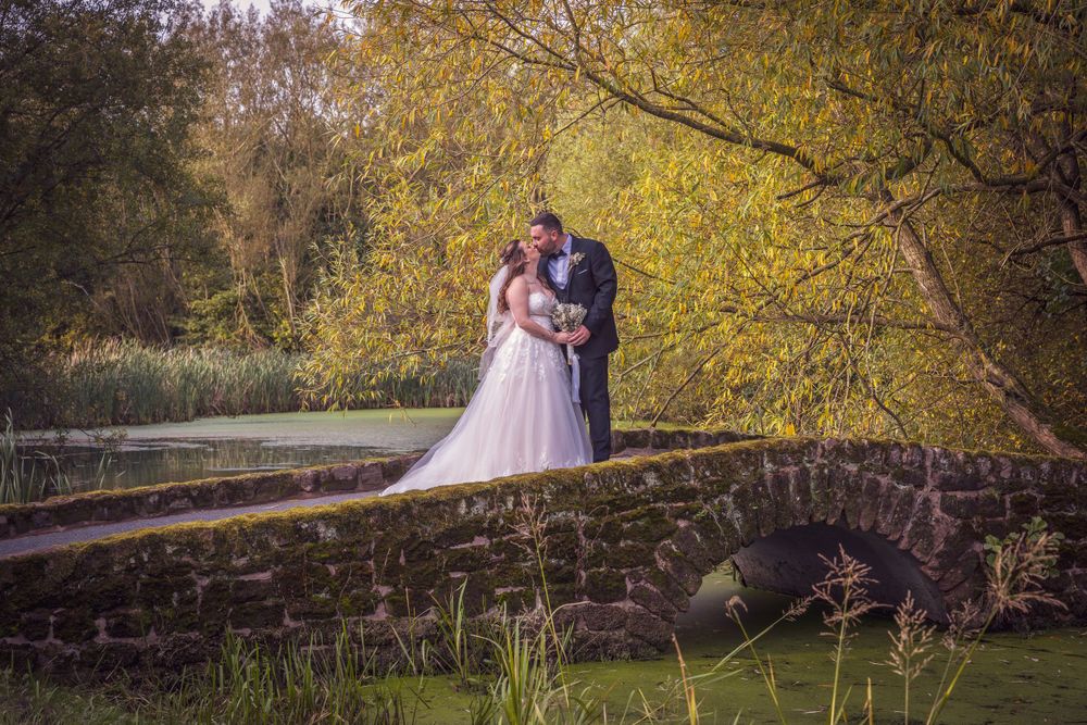 Bride and groom share romantic moment on stone bridge surrounded by autumn trees.
