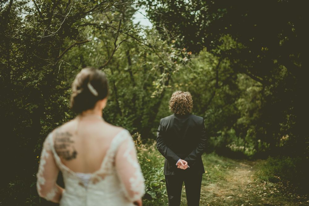 Two figures walk along a wooded forest path surrounded by lush green foliage on a summer day.