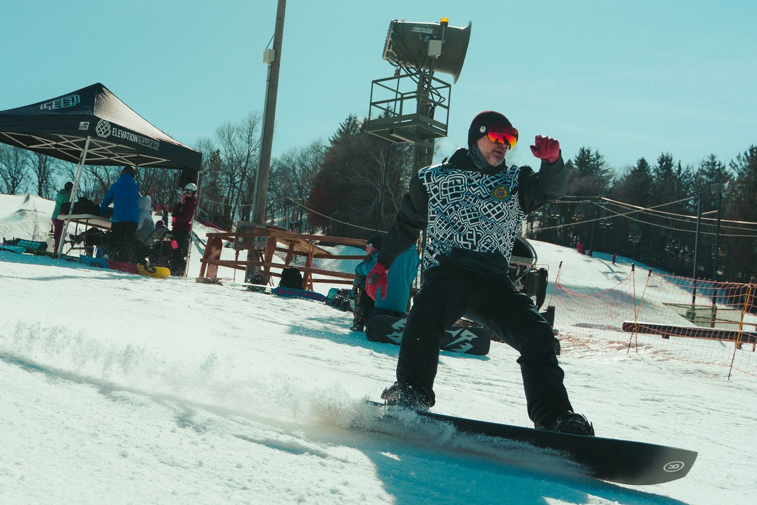 Snowboarder performing trick at winter ski resort with lift tower in background.