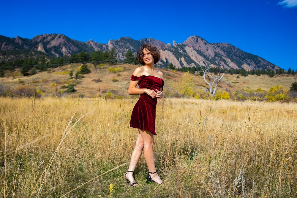 A series of photos showing someone in a red dress posing in a golden field with the Flatirons mountains of Boulder, Colorado.