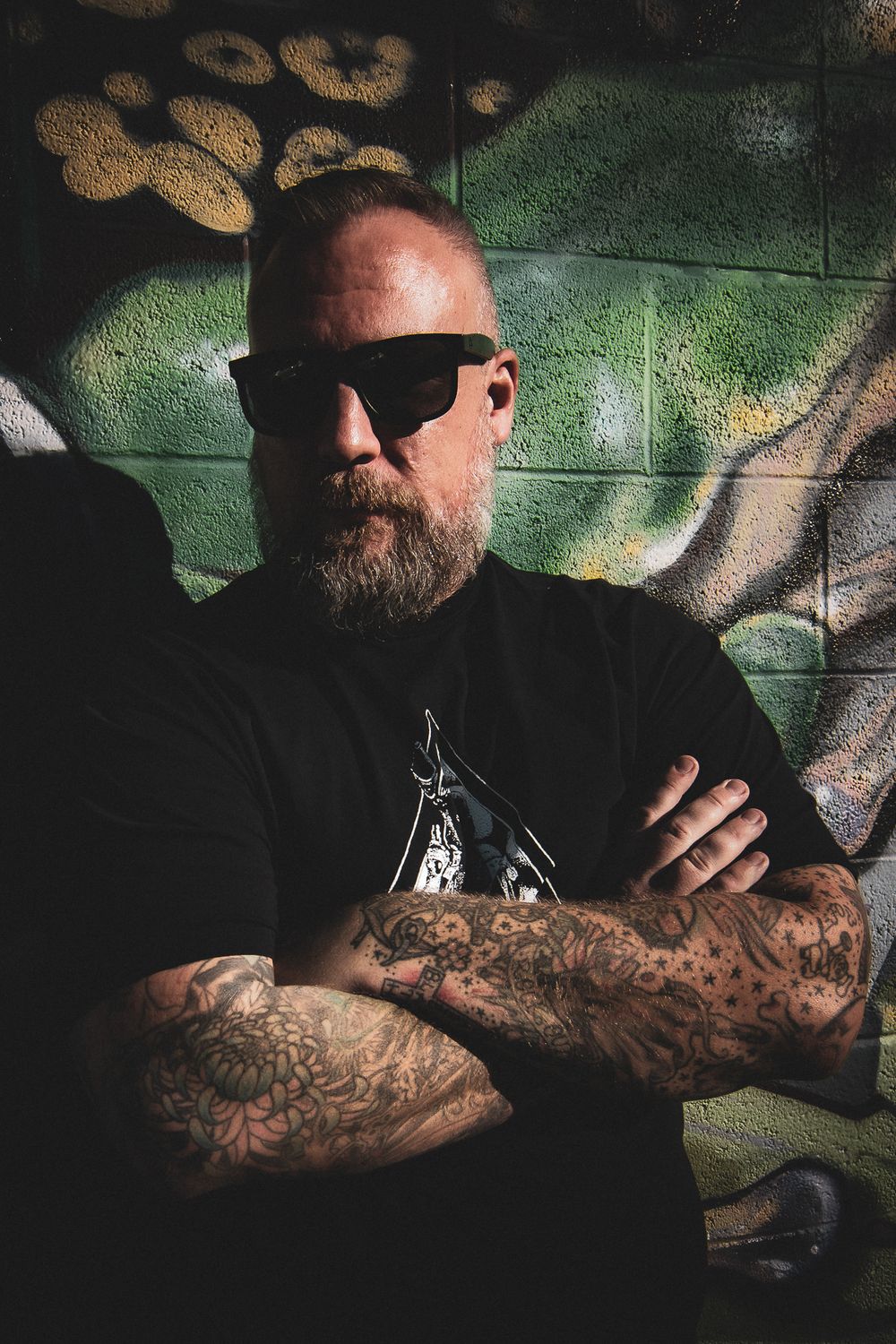 A series of photos showing heavily tattooed arms against a green and white graffiti wall background.