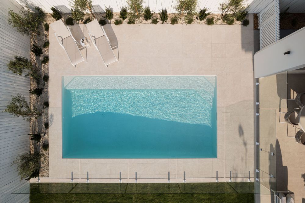 Aerial view of a rectangular swimming pool surrounded by concrete decking and landscaped garden beds.
