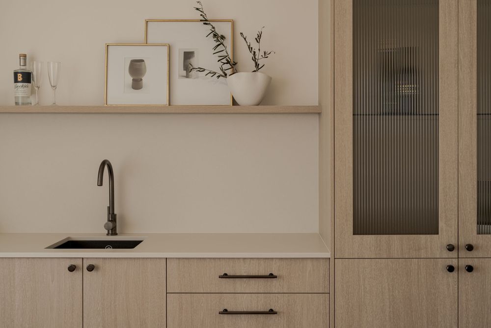 Minimalist kitchen design with light wood cabinets, black fixtures, and decorative shelf styling.