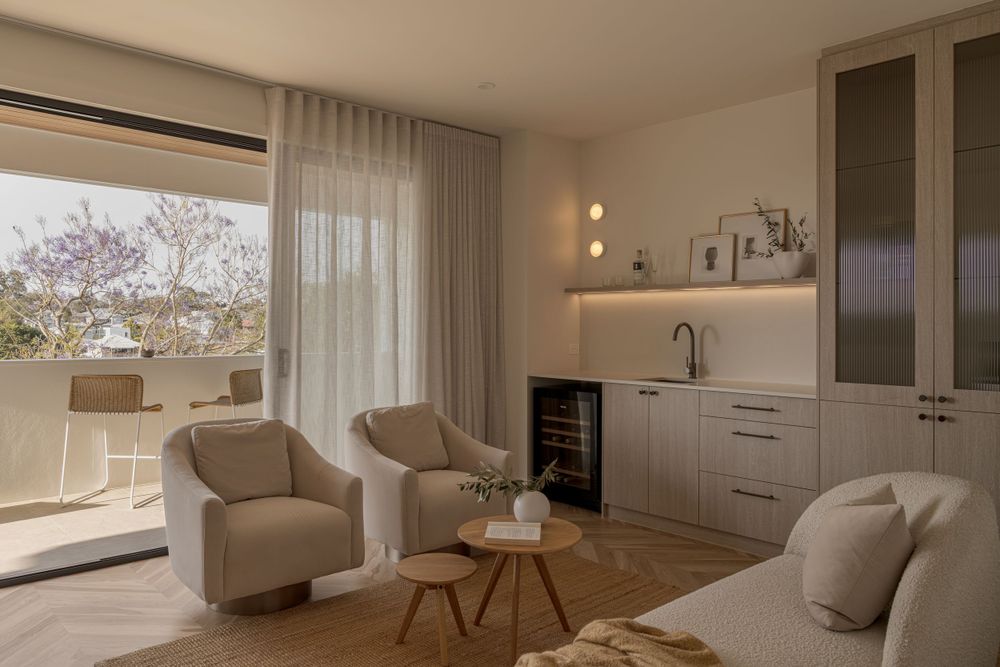 Modern living space with built-in cabinetry, beige armchairs, and floor-to-ceiling windows with sheer drapes.
