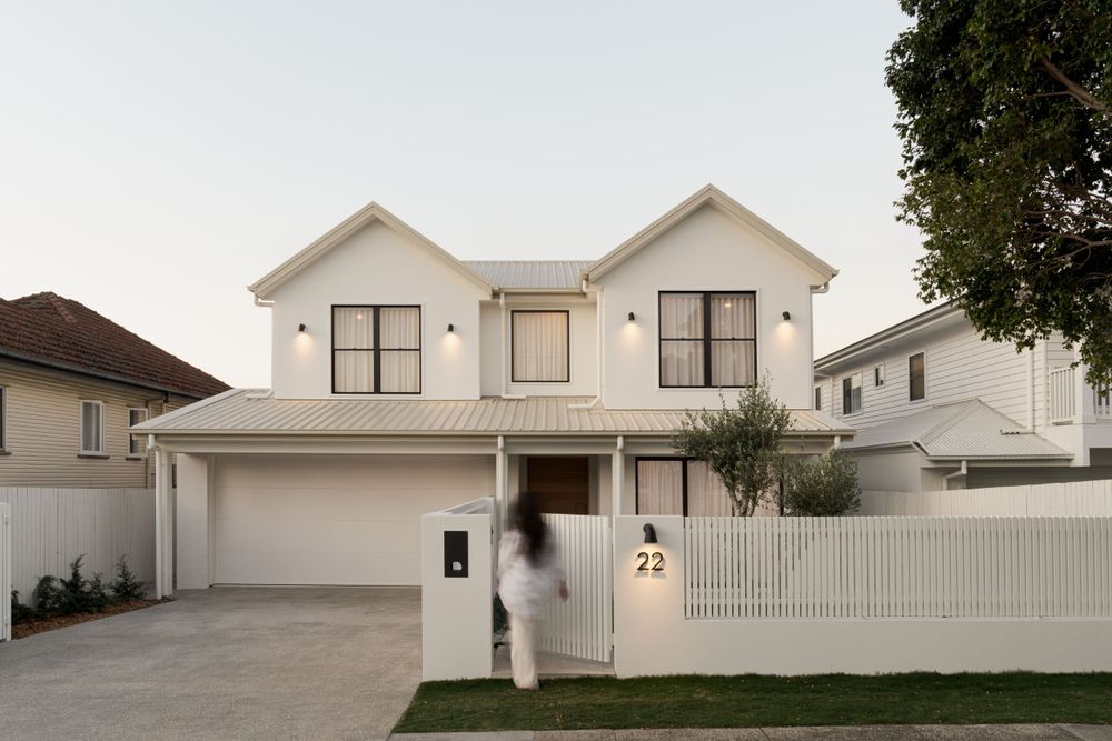 White Hampton-style house with double garage, pitched rooflines, and classic white picket fence.