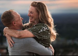 A joyful couple embraces and laughs together outdoors at sunset, sharing a warm and loving moment.