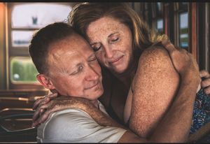Middle-aged couple sharing a warm embrace, smiling tenderly inside a cozy indoor setting.