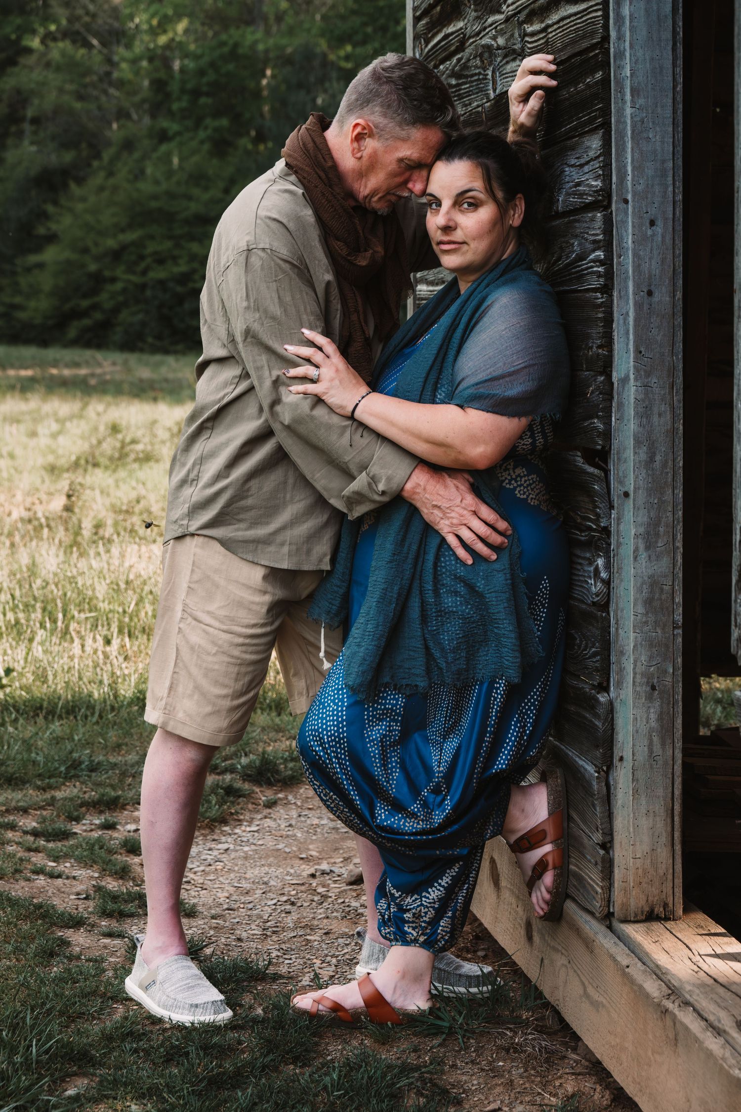 Loving couple embracing tenderly against a stone wall in a lush green field.