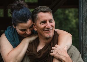 Joyful couple sharing a tender moment, woman hugging man from behind outdoors.