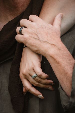 Close-up of couple's intertwined hands wearing wedding rings, symbolizing love.