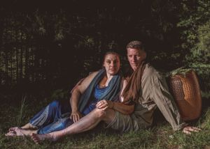 Couple sitting together on grass in a wooded area during an outdoor photo session.