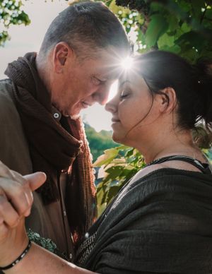 Romantic couple facing each other with sunlight glowing between them outdoors.