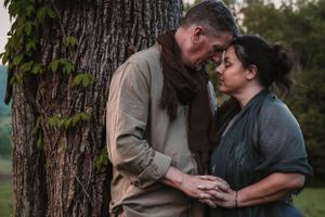 Romantic couple leaning foreheads together beside a tree trunk in a serene outdoor setting.