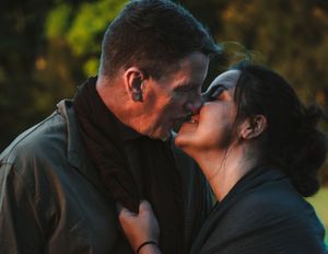 Couple sharing a kiss outdoors in warm golden light in a romantic close-up portrait.