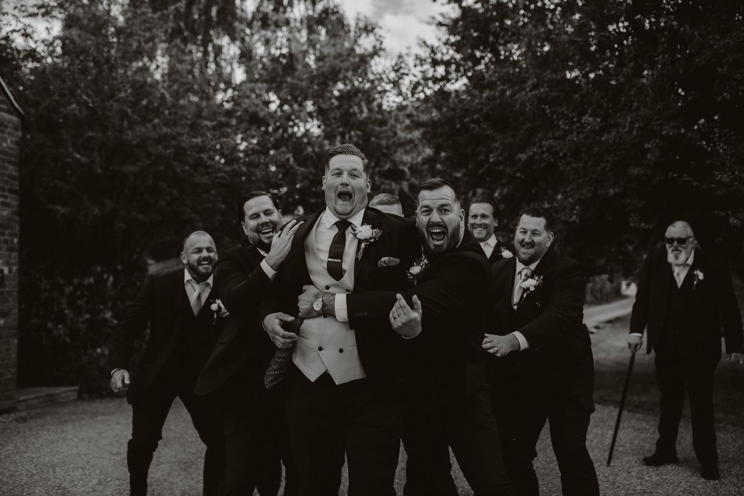 Black and white group photo of groomsmen celebrating outdoors. Houchins Essex photographer