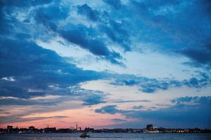 Dramatic blue and pink sunset sky over a calm waterfront with city skyline silhouette and clouds.