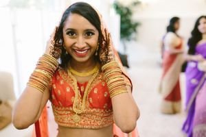 Indian bride in red and gold lehenga with bangles and dupatta smiling at her wedding ceremony.