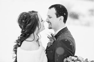 Black and white winter wedding photo of smiling bride and groom in snow, bride holding bouquet.
