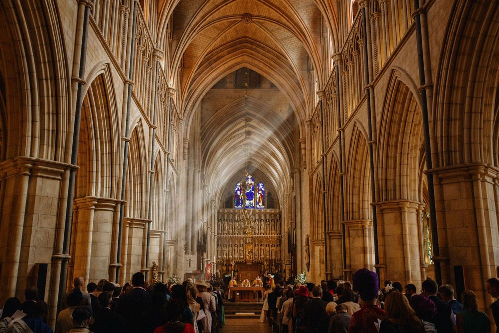 Sunlight pours into Southwark cathedral with soaring ribbed vaulting and pointed arches. Wedding ceremony with guests seated