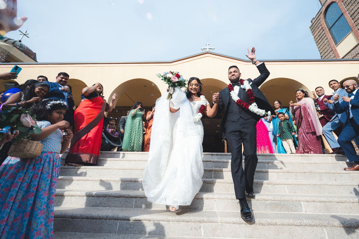 Newlyweds joyfully exit down church steps surrounded by celebrating guests.