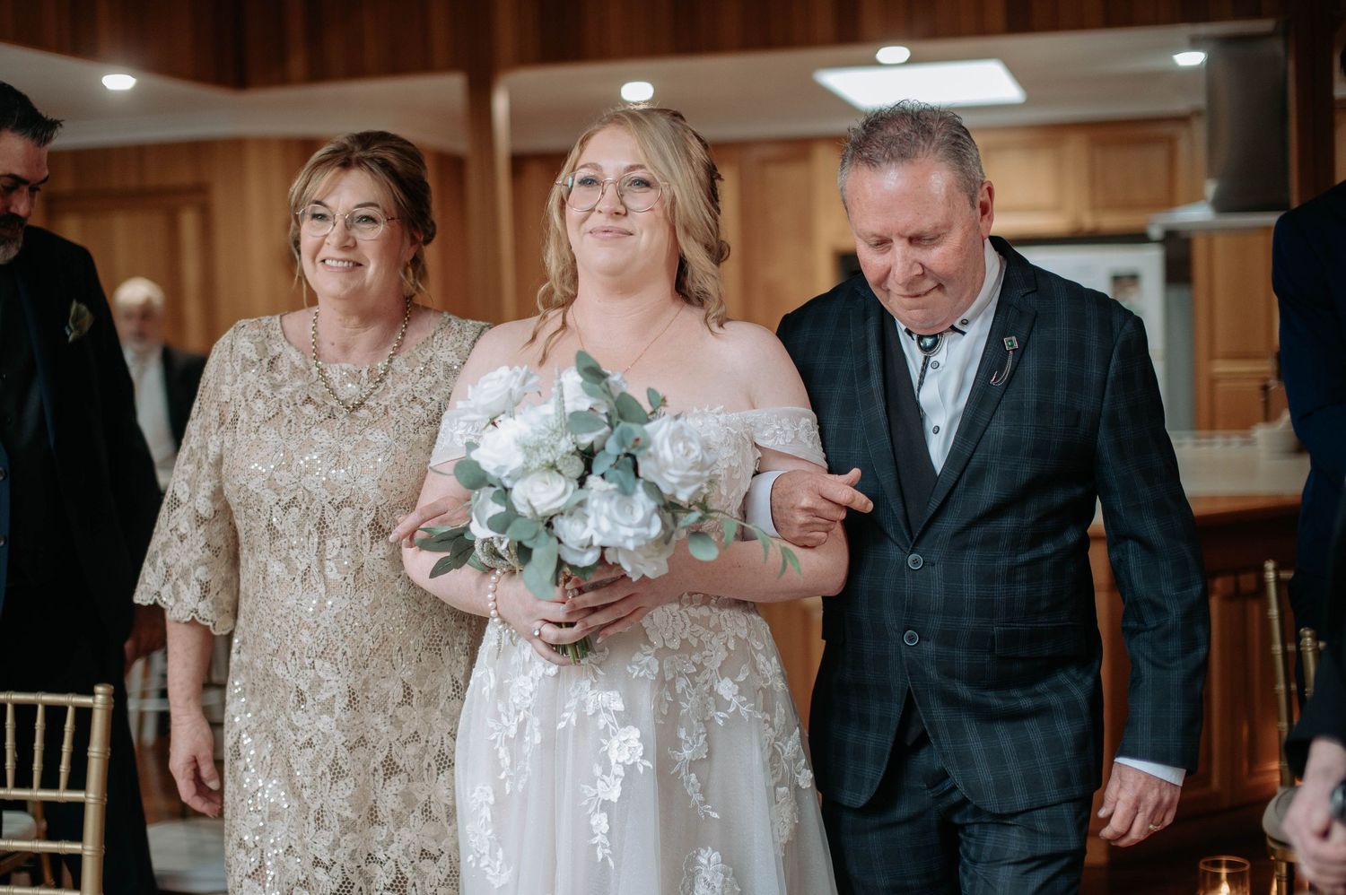 A wedding processional moment in a wood-paneled venue with natural light.