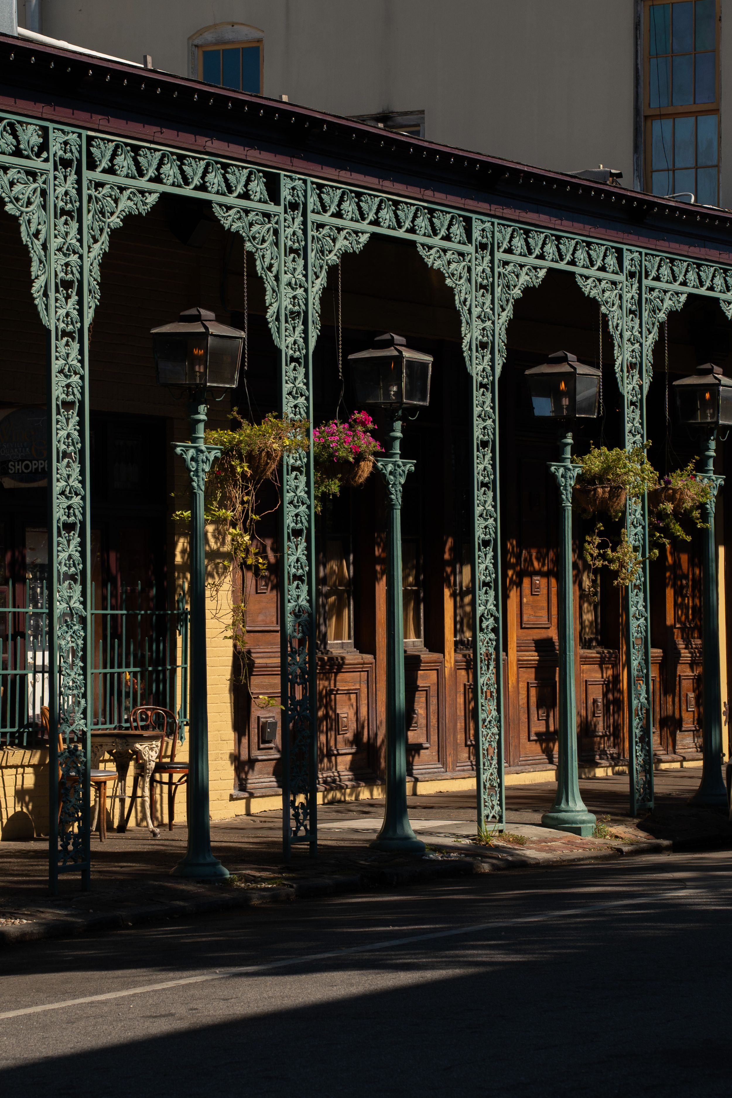 Ornate green metal archways with hanging lanterns and flower baskets line a historic street corridor.