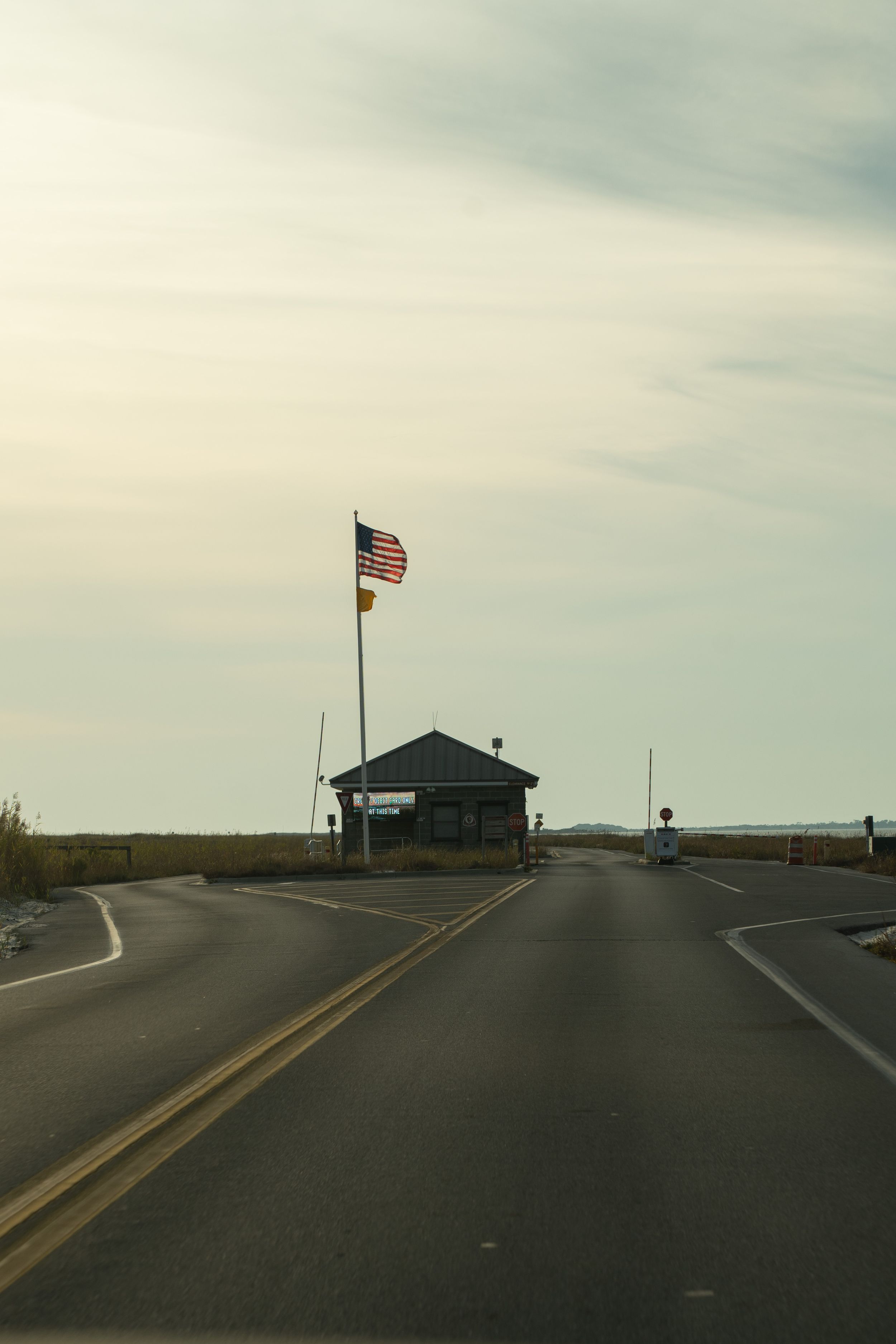 A small guard station with an American flag stands at a fork in a coastal road under an overcast sky.