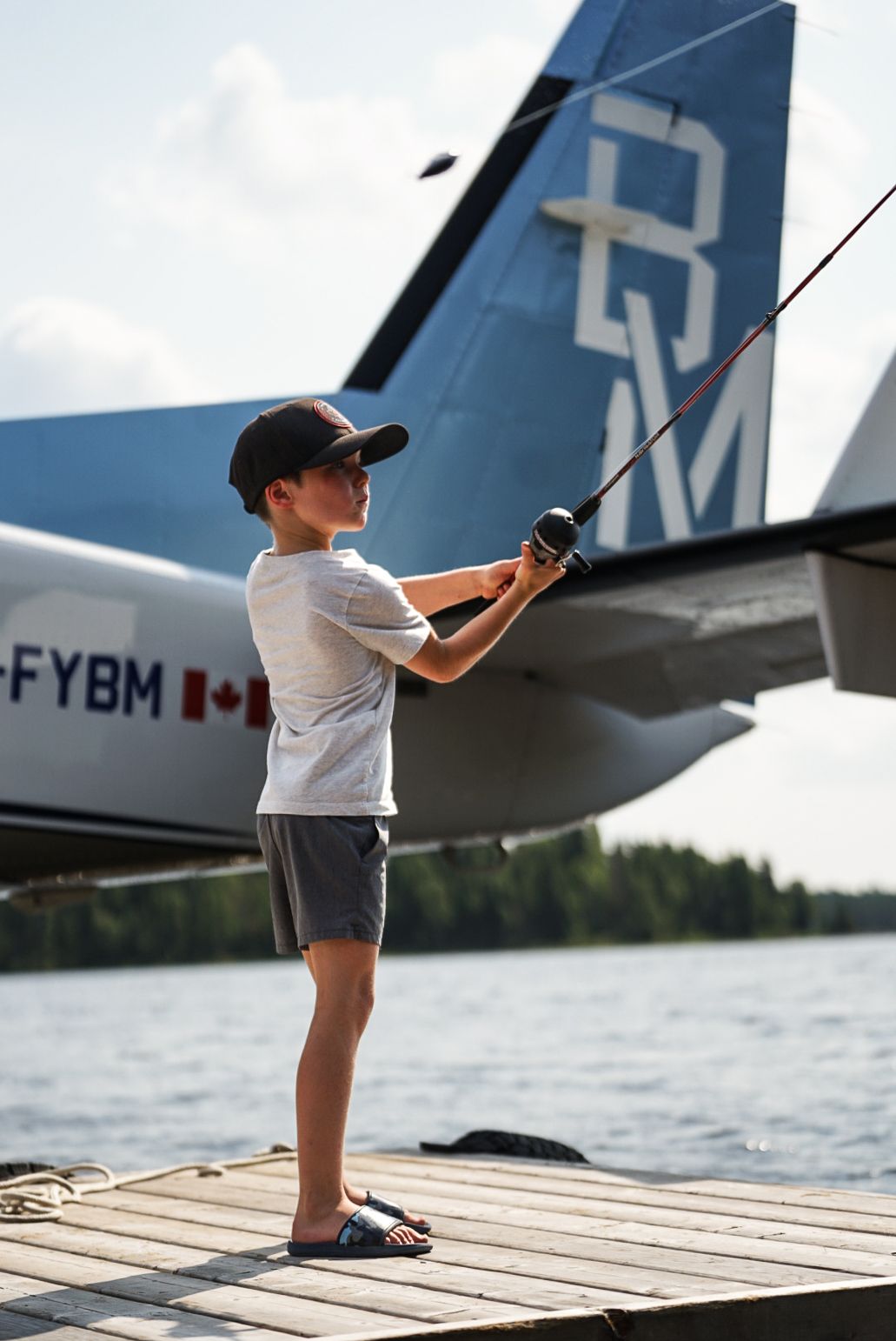 Young angler fishing from wooden dock near seaplane tail.