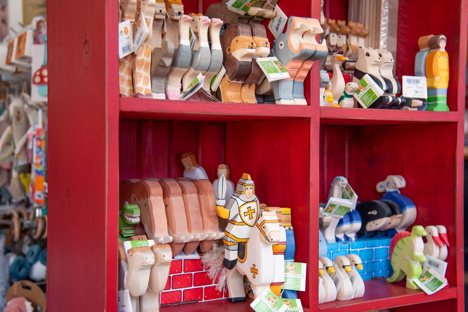 Colorful wooden toy figures and animals displayed on bright red shelves in a traditional shop setting.