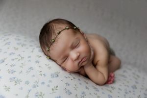 Sleeping newborn baby wearing a delicate gold headband rests peacefully on floral patterned fabric.