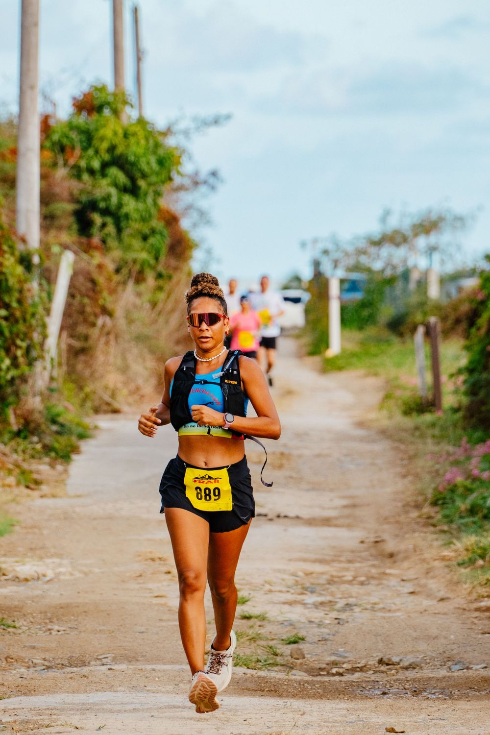 Runner wearing sunglasses and yellow shorts competes on a dirt trail during a marathon race on a sunny day.