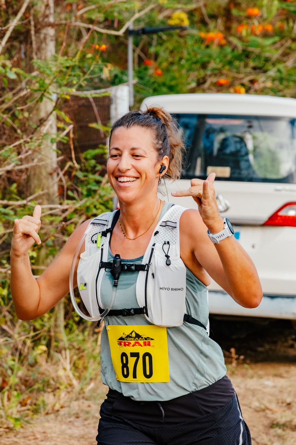 Happy trail runner celebrating with bib number 870 during outdoor race with parked car in background.