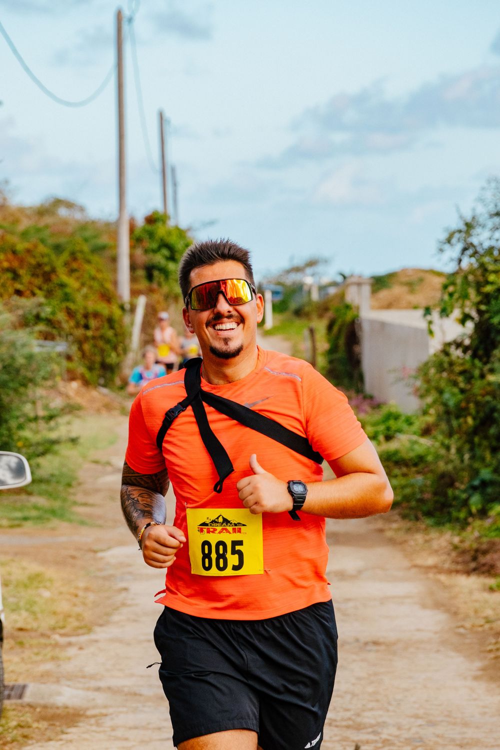 Runner in bright orange shirt and reflective sunglasses wearing race number 885 during a trail race competition.