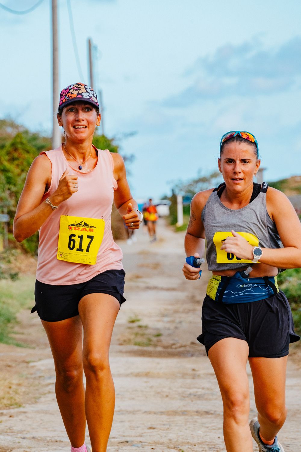 Runners with race bibs competing in a marathon on a dirt path under blue skies.