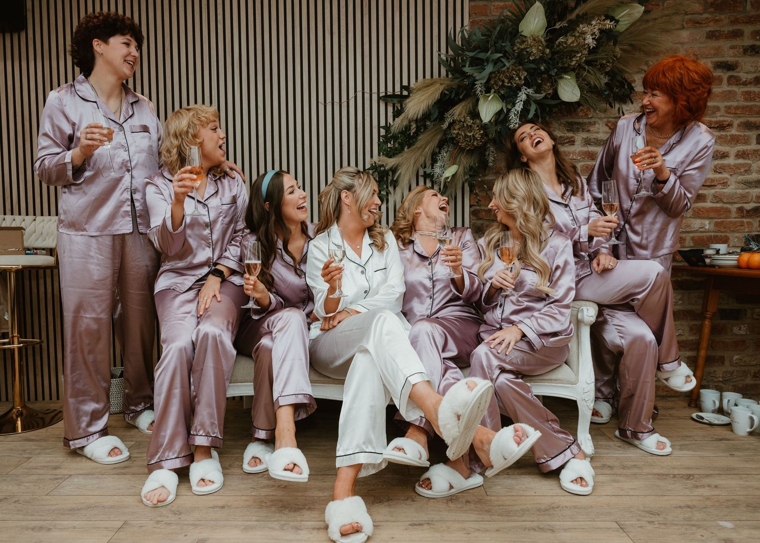 Group wearing matching silk pajamas celebrate during pre-wedding preparations.