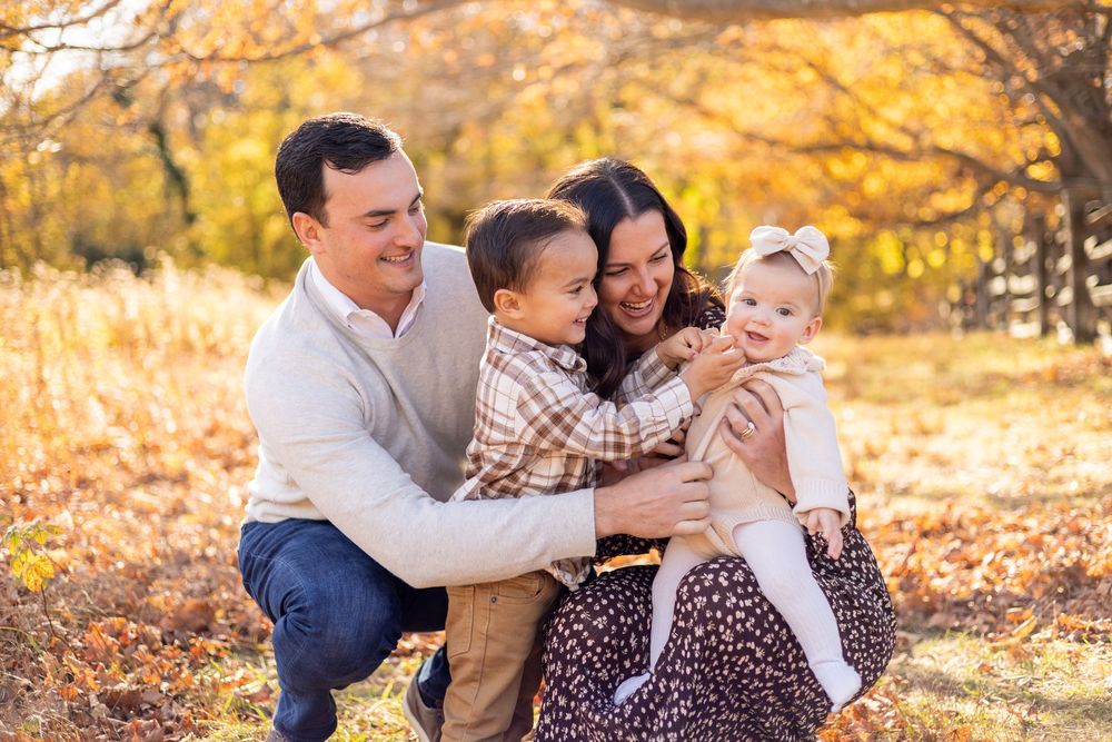 Happy family of four laughing and embracing in fall foliage outdoors.