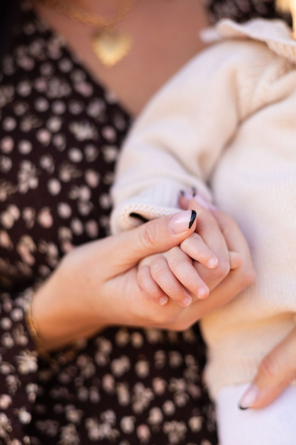 Close-up of mother gently holding tiny baby fingers in autumn light.