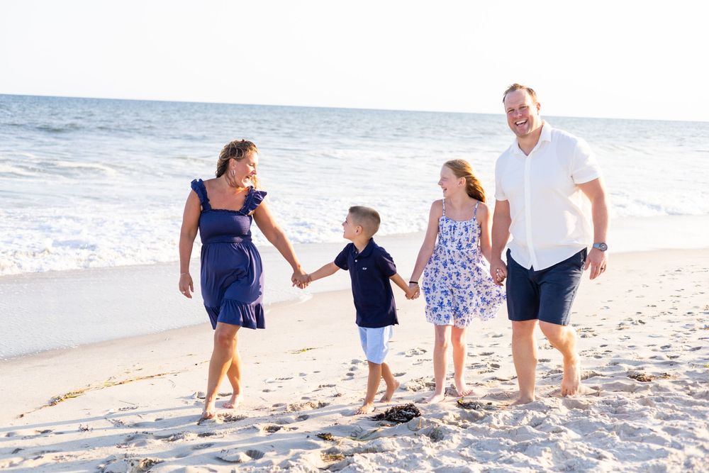Happy family of four holding hands and walking together on a sunny beach.