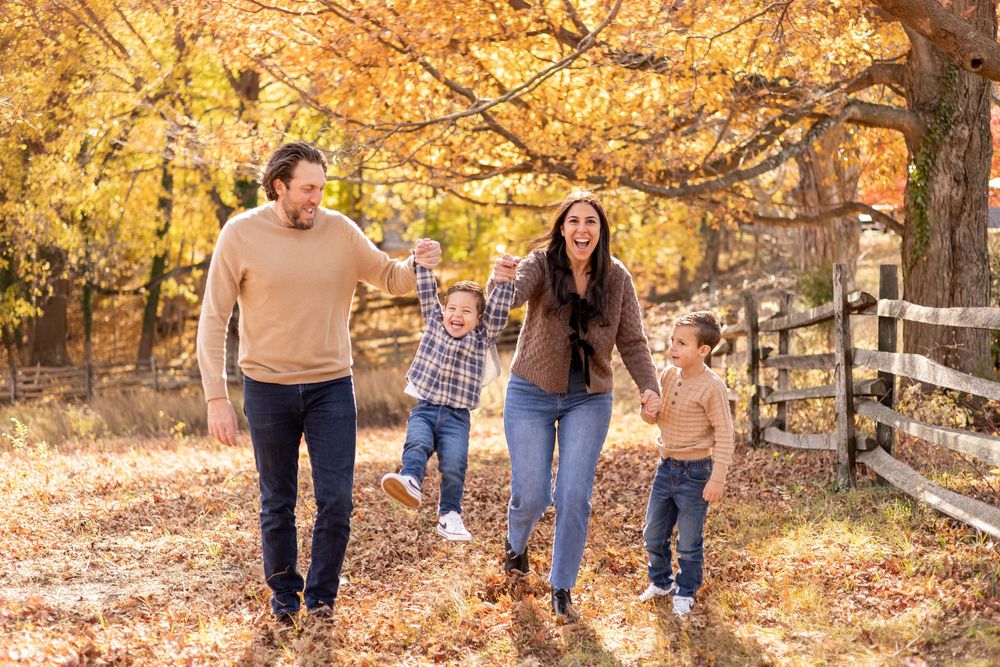 Joyful family swinging young child between parents while walking through a golden autumn park.