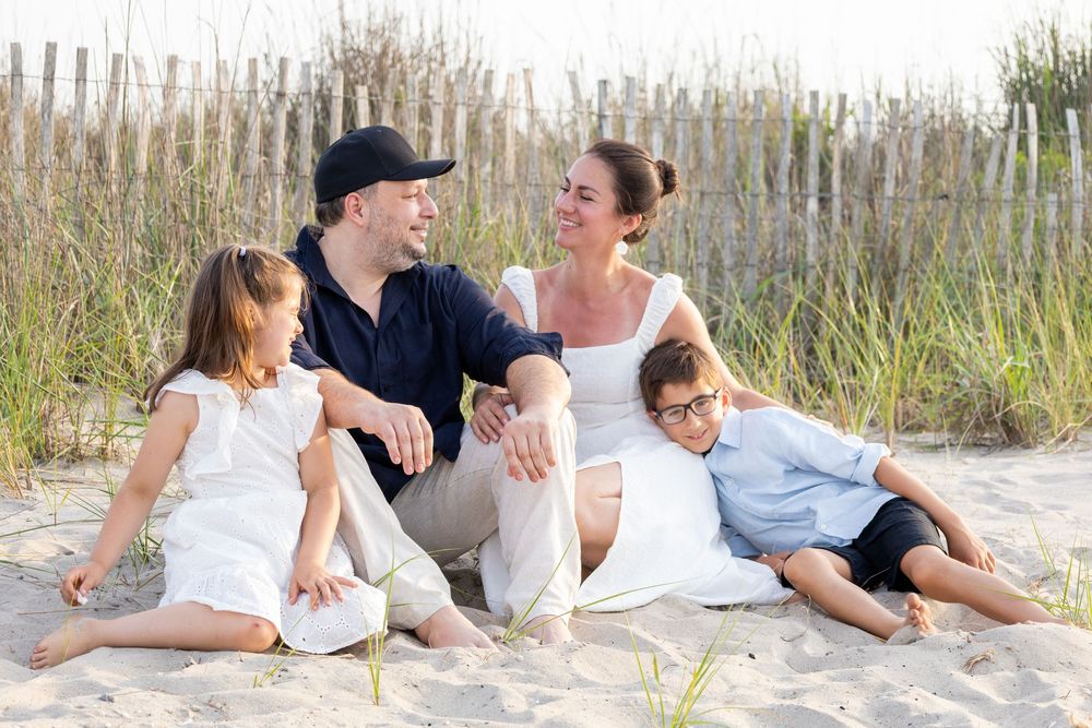 Happy family of four relaxes together on sandy beach dunes on a sunny day.