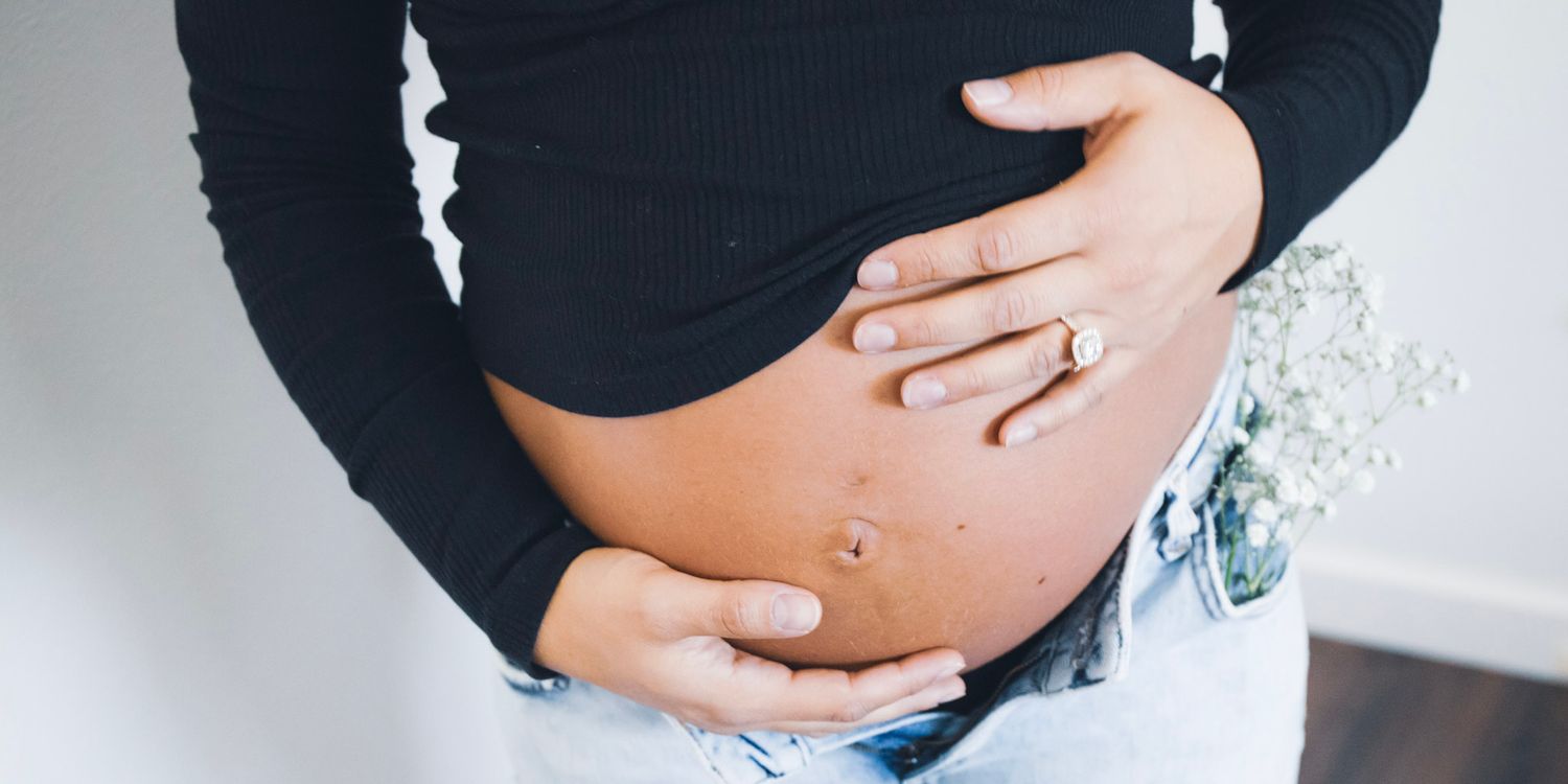 Close up view of a pregnant belly with hands gently cradling the bare baby bump, wearing a black long sleeve top.