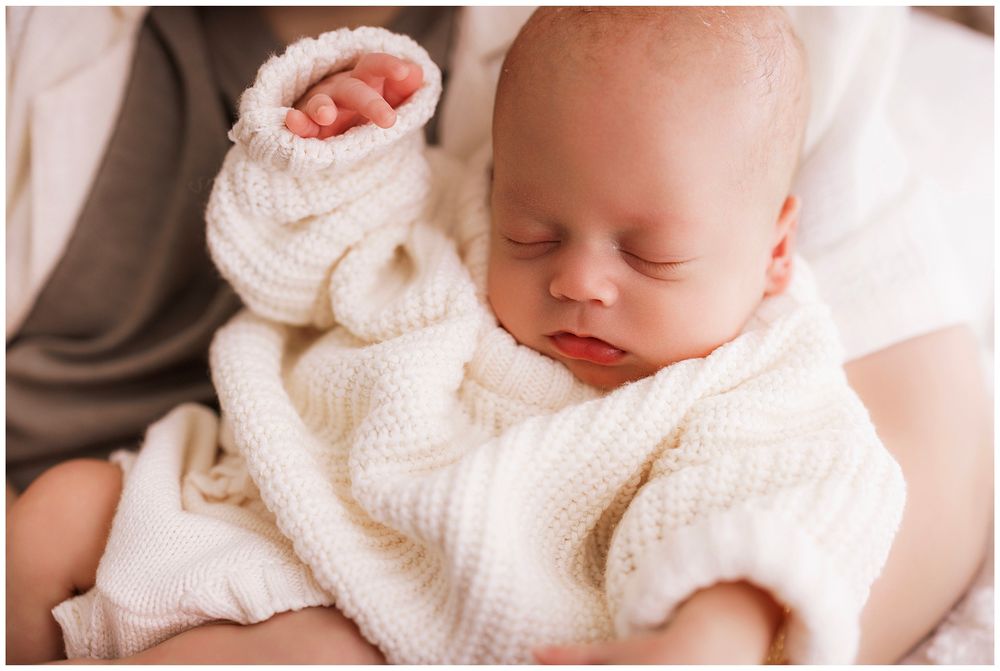 A peaceful sleeping infant wearing a cozy white knit sweater rests on soft bedding.