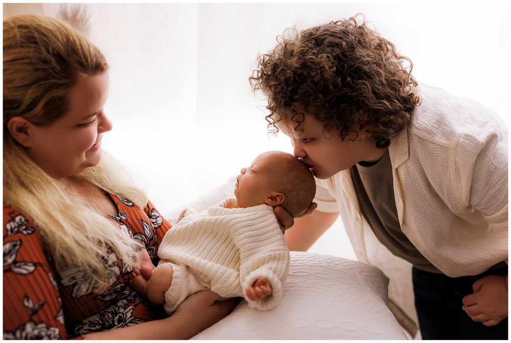 An intimate newborn photography session showing tender moments with a sleeping baby wrapped in soft white blankets.