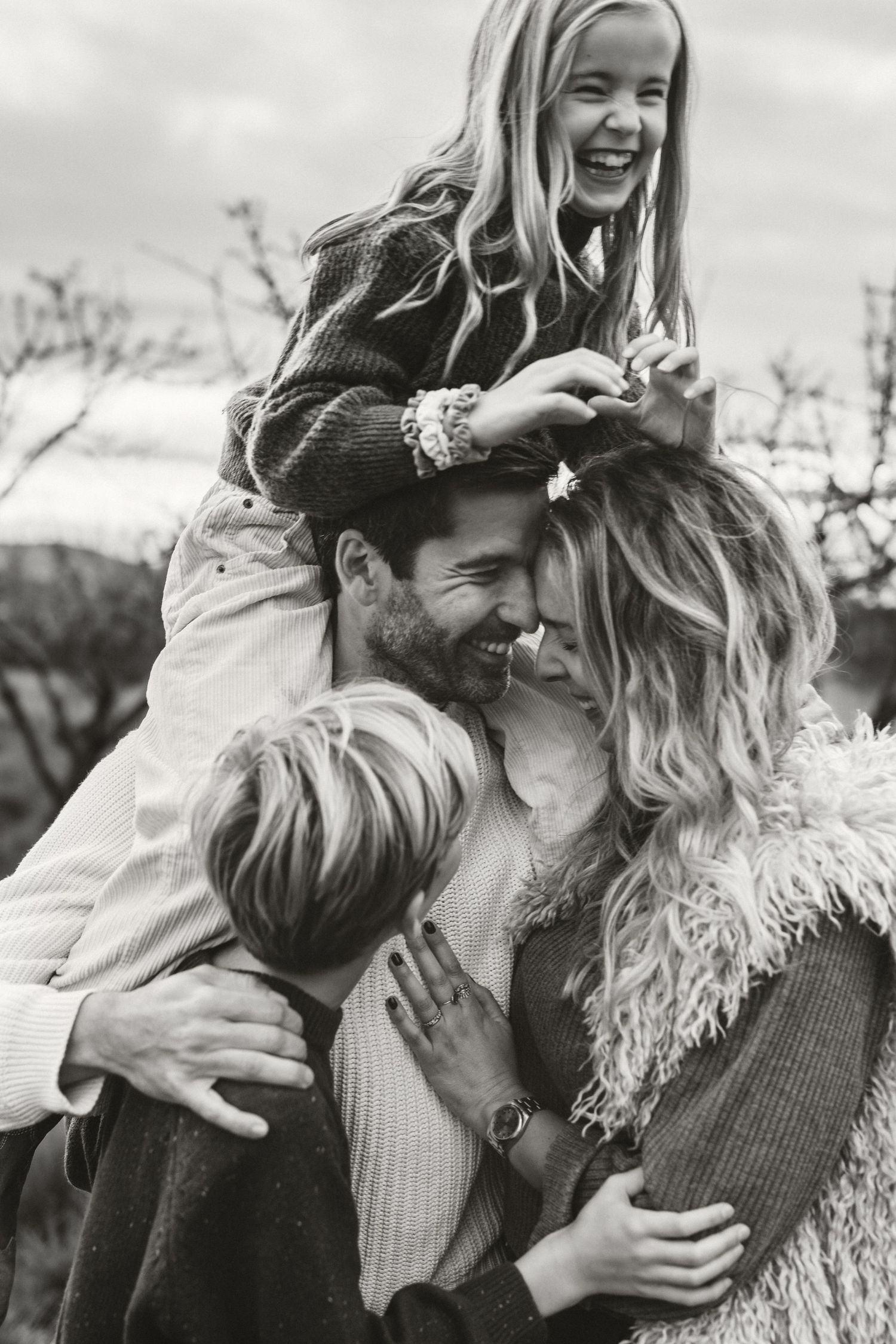 Black and white candid photograph showing a joyful family moment with children and parents embracing and laughing outdoors in Javea Photo