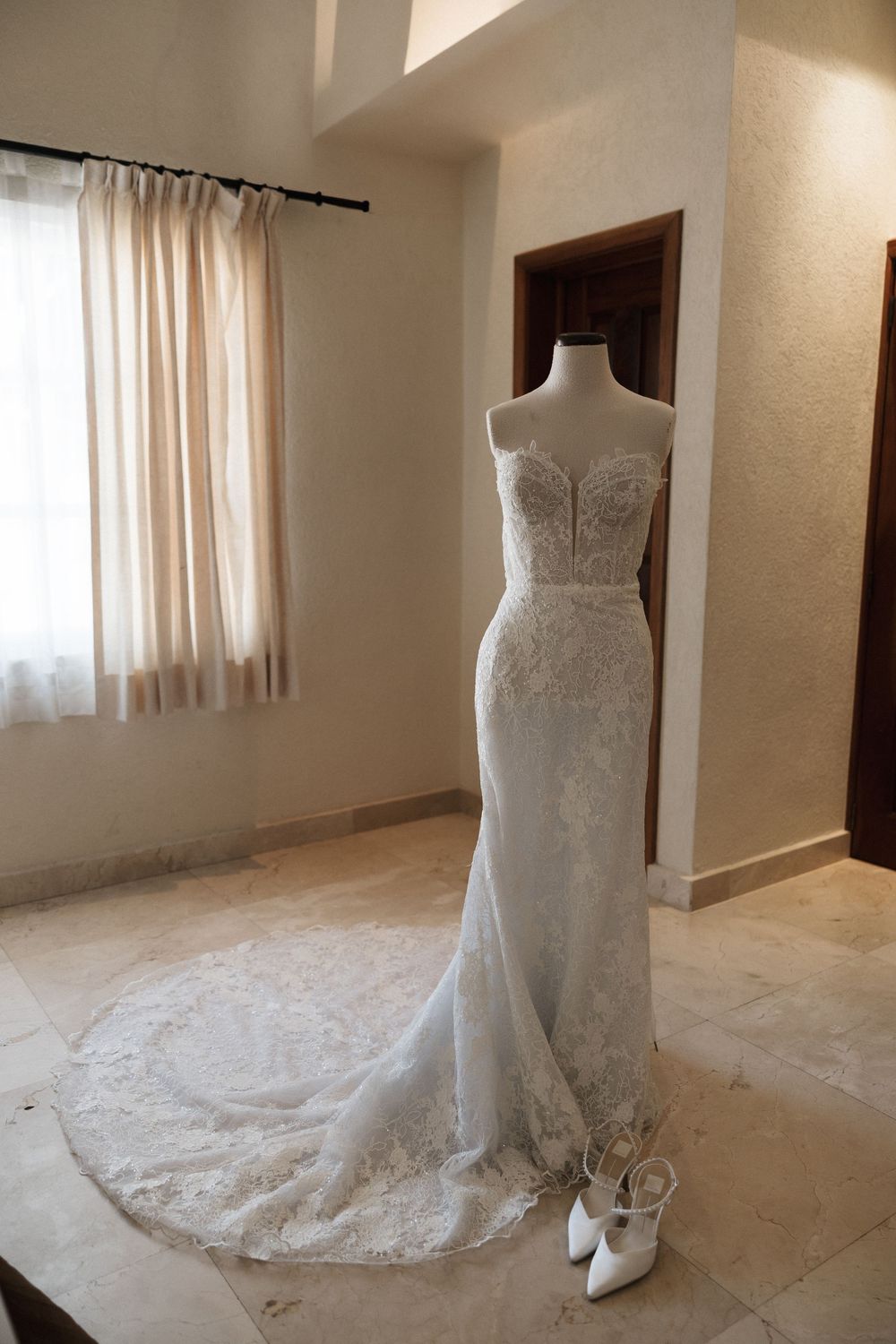 Elegant white lace wedding dress on mannequin with sweetheart neckline and long train displayed with bridal shoes.